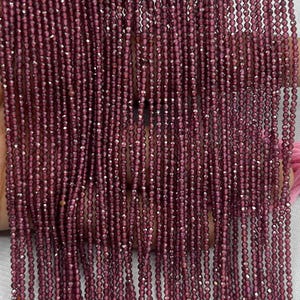 May include: Strands of faceted, deep burgundy beads. The beads are strung together, creating a curtain-like effect. The beads have a sparkling, reflective quality, suggesting they are made of a gemstone or crystal. The overall effect is elegant and luxurious.