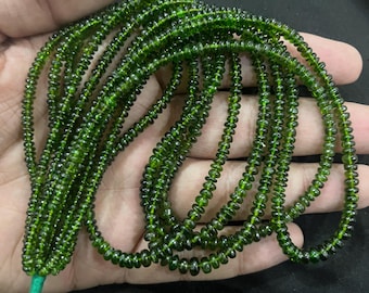 Puede incluir: Múltiples hebras de pequeñas cuentas redondas de color verde oscuro. Las cuentas están ensartadas, formando múltiples hebras. Las cuentas tienen una superficie pulida y reflectante. Las hebras se mantienen unidas con un hilo verde. Las cuentas son de un color verde intenso y rico.