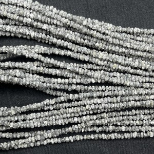 May include: A strand of gray rough diamond beads. The beads are small and irregular in shape, and they are strung together on a clear thread.