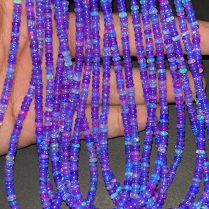 May include: Strands of purple opal beads with iridescent flashes of color. The beads are small and round, strung together to create a necklace or bracelet. The opals have a mix of blue, pink, and green hues.