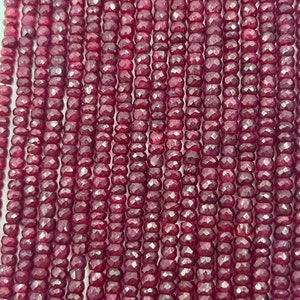 May include: A strand of deep red ruby beads, each bead is faceted and has a slightly irregular shape. The beads are strung on a clear thread and are ready to be used for jewelry making.