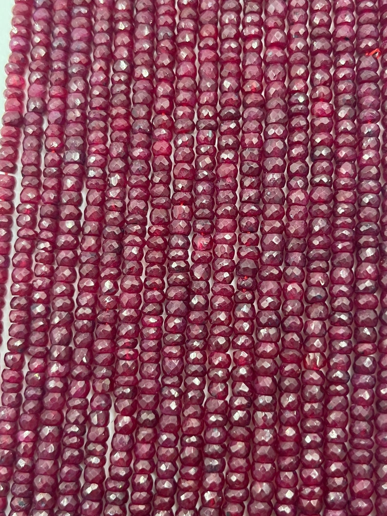 May include: A strand of deep red ruby beads, each bead is faceted and has a slightly irregular shape. The beads are strung on a clear thread and are ready to be used for jewelry making.