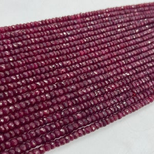 May include: A strand of deep red ruby beads, each bead is faceted and has a slightly irregular shape. The beads are strung on a clear thread and are arranged in a straight line.