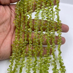 Könnte beinhalten: Eine Strähne grüner Peridot-Perlen, facettiert und oval geformt. Die Perlen sind auf einem durchsichtigen Faden aufgereiht und haben einen Durchmesser von etwa 6 mm.