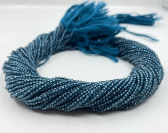 May include: A strand of blue gemstone beads, likely faceted, with a shimmery finish. The beads are strung together and arranged in a coil shape.