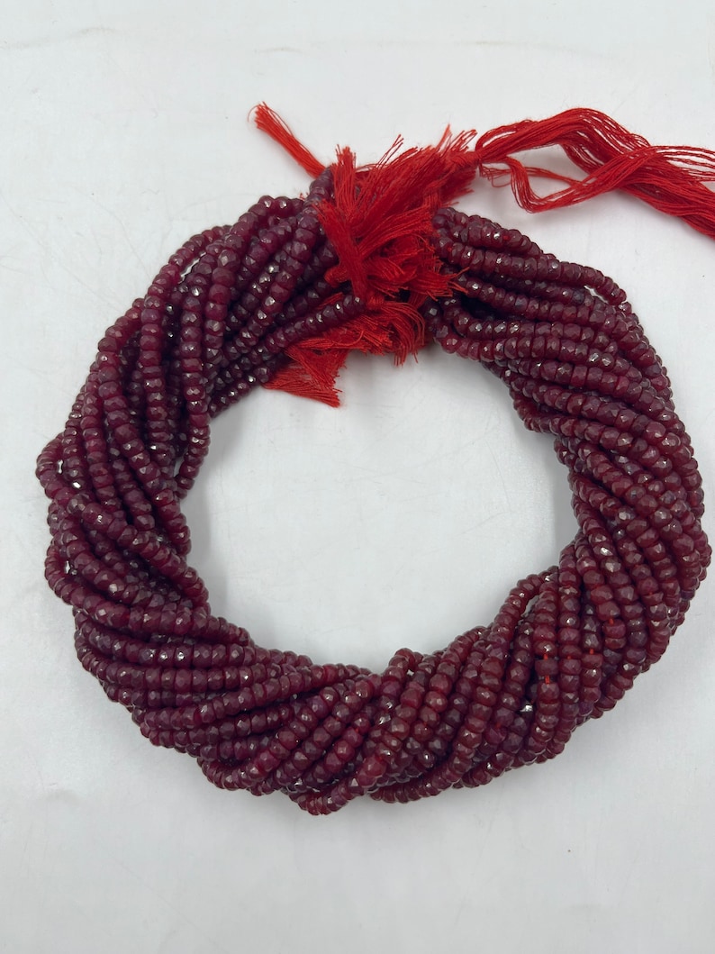 May include: A strand of deep red faceted gemstone beads. The beads are small and uniform in size, and the strand is long enough to make a necklace or bracelet.