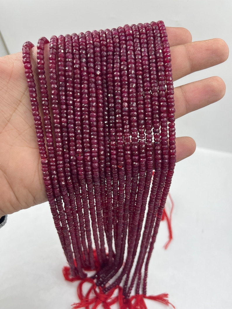 May include: A strand of deep red ruby beads, faceted and strung on a thin thread. The beads are small and uniform in size, creating a continuous line of color.