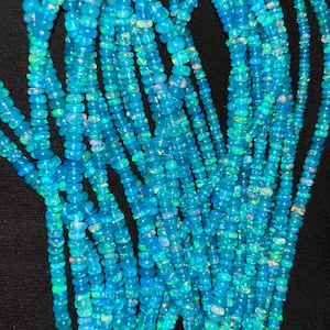 May include: A strand of blue opal beads, with a smooth, rounded shape. The beads are strung on a clear thread and are ready to be used for jewelry making.