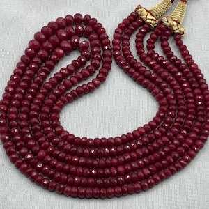 May include: A multi-strand necklace with faceted, deep red beads. The necklace has a layered design, with several strands of beads cascading down. The ends of the necklace are finished with gold-coloured accents.
