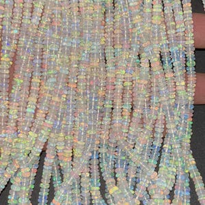 May include: A strand of white opal beads with iridescent rainbow flashes. The beads are small and oval shaped.