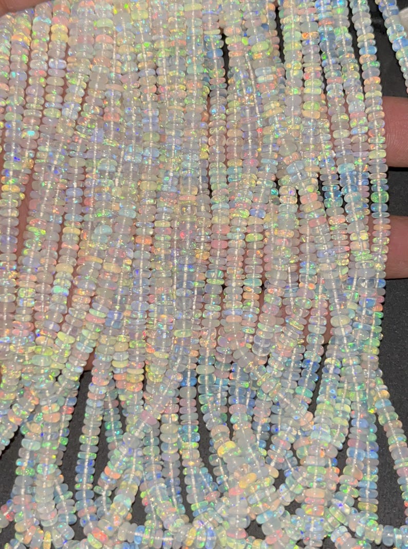 May include: A strand of white opal beads with iridescent rainbow flashes. The beads are small and oval shaped.