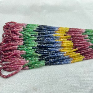 May include: A strand of colourful gemstone beads, including red, pink, green, blue, and yellow. The beads are small and uniform in size, and they are strung together on a clear thread.