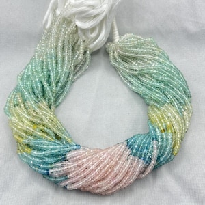 Puede incluir: Un collar de múltiples hilos con un degradado de colores. El collar pasa del blanco al verde claro, amarillo, azul y rosa. Los hilos se mantienen unidos por una borla blanca.