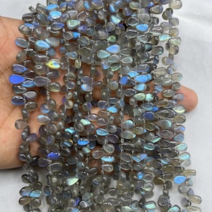 Puede incluir: Hebras de cuentas de piedras preciosas de labradorita gris con destellos iridiscentes azules y verdes. Las cuentas en forma de lágrima están ensartadas, creando un efecto brillante. Adecuado para la fabricación de joyas.
