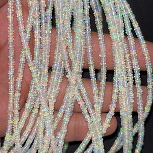 May include: Strands of small, iridescent opal beads. The beads are strung together, creating a shimmering effect. The opals display a range of colors, including white, blue, green, and yellow. The beads are small and uniform in size, suitable for jewelry making.