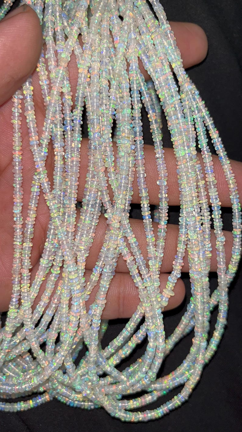 May include: Strands of small, iridescent opal beads. The beads are strung together, creating a shimmering effect. The opals display a range of colors, including white, blue, green, and yellow. The beads are small and uniform in size, suitable for jewelry making.