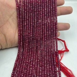 May include: A strand of deep red ruby beads, faceted and round, strung on a thin thread. The beads are uniform in size and have a smooth, polished finish.