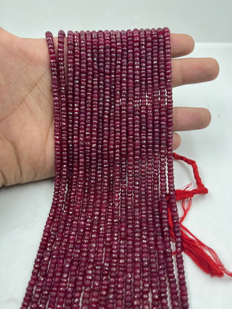 May include: A strand of deep red ruby beads, faceted and round, strung on a thin thread. The beads are uniform in size and have a smooth, polished finish.