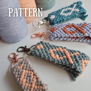 Może przedstawiać: Zbliżenie ręcznie robionych breloków z makramy w różnych kolorach, w tym turkusowym, szarym i brzoskwiniowym. Breloki mają geometryczne wzory i metalowe zapięcia. Słowo "PATTERN" jest widoczne w białym tekście. Kłęby przędzy w pasujących kolorach w tle.