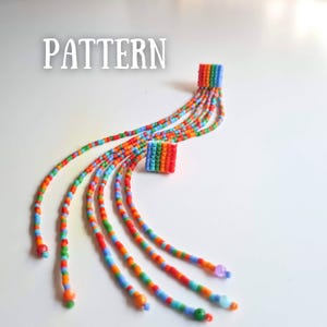 May include: A vibrant beaded accessory with the word "PATTERN" in white. It features a square base and multiple strands of rainbow-coloured beads. The strands are made of small beads in red, orange, yellow, green, blue, and purple, each ending with a single bead.