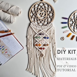 Könnte beinhalten: DIY-Set für eine Makramee-Wandbehänge mit einem Holzmandala mit dem Om-Symbol. Das Set enthält weißes Garn, sieben Chakra-Kristalle, einen goldenen Om-Anhänger und ein PDF- und Video-Tutorial.