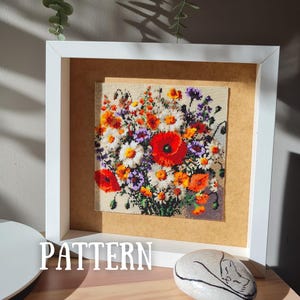 May include: A square white frame containing a beaded artwork of a vibrant wildflower bouquet. The floral arrangement features bright red poppies, white daisies, and small purple and orange blossoms on a light background. The word PATTERN is visible.