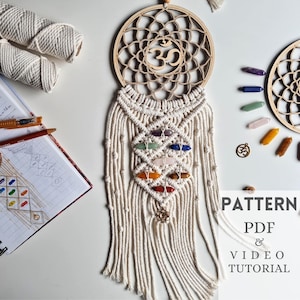 May include: A white macrame wall hanging with a wooden circle featuring the Om symbol and seven colourful crystals. The hanging is accompanied by a pattern and video tutorial for creating a similar piece.