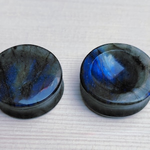 May include: Pair of round, dark blue and grey stone ear gauges. The gauges have a smooth, polished finish.