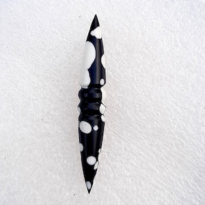 May include: A black and white, pointed,  stone pendant with a swirling pattern.