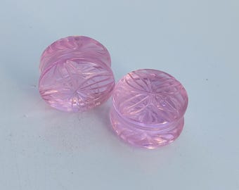 May include: Two pink glass ear gauges with a carved floral design.
