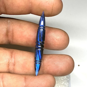 Pode incluir: Uma gema de labradorita azul escura e preta esculpida em forma pontiaguda, que se assemelha a uma bala.