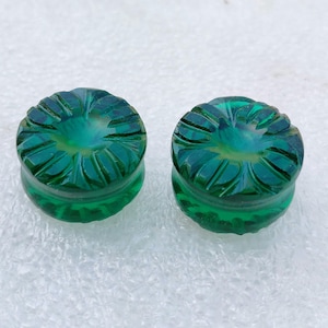 Może przedstawiać: Dwa okrągłe guziki ze szkła w kolorze zielonym z rzeźbionym wzorem kwiatu.