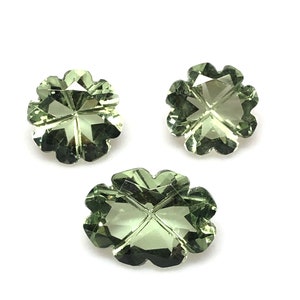 May include: Three green gemstone clover-shaped cabochons. The gemstones are faceted and have a translucent appearance.