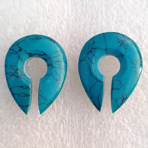 May include: A pair of turquoise blue ear gauges with a teardrop shape and a hole in the center. The gauges have a marbled pattern.