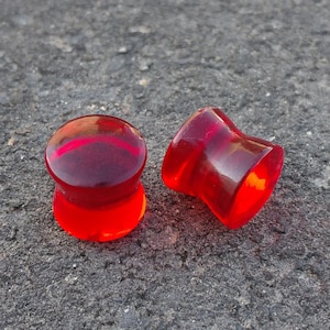 May include: Two red acrylic ear gauges, one is a simple cylinder shape and the other is a flared cylinder shape.