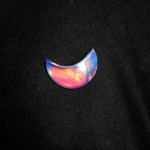 Pode incluir: Um cabochão de opala iridescente em forma de crescente com um esquema de cores rosa, azul e roxo.