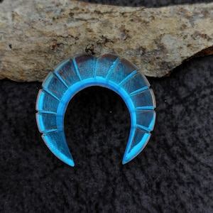 Op de afbeelding: Een blauwe glazen hoefijzervormige hanger met een getextureerd oppervlak.