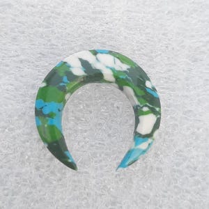 Puede incluir: Un expansor de oreja en forma de media luna marmoleado en verde, azul y blanco.