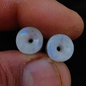 May include: Two white moonstone beads with a hole in the center. The beads are iridescent and have a smooth, polished finish.
