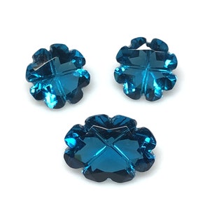 May include: Three blue topaz gemstones in a clover shape. The gemstones are faceted and have a deep blue color.