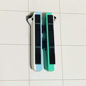 May include: Two Nintendo Switch Joy-Con controllers, one white and blue, the other green. The controllers are side-by-side and have black buttons.