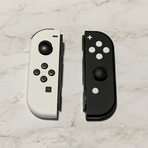 Puede incluir: Dos mandos Joy-Con para Nintendo Switch, uno blanco y otro negro. Ambos mandos tienen los botones y las palancas anal&oacute;gicas est&aacute;ndar.