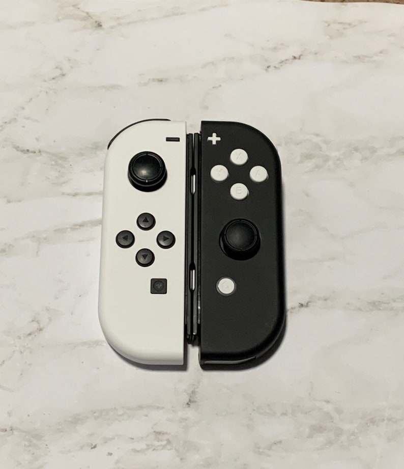 Puede incluir: Un mando de Nintendo Switch blanco y negro con un dise&ntilde;o dividido. El lado izquierdo es blanco con botones negros y el lado derecho es negro con botones blancos.