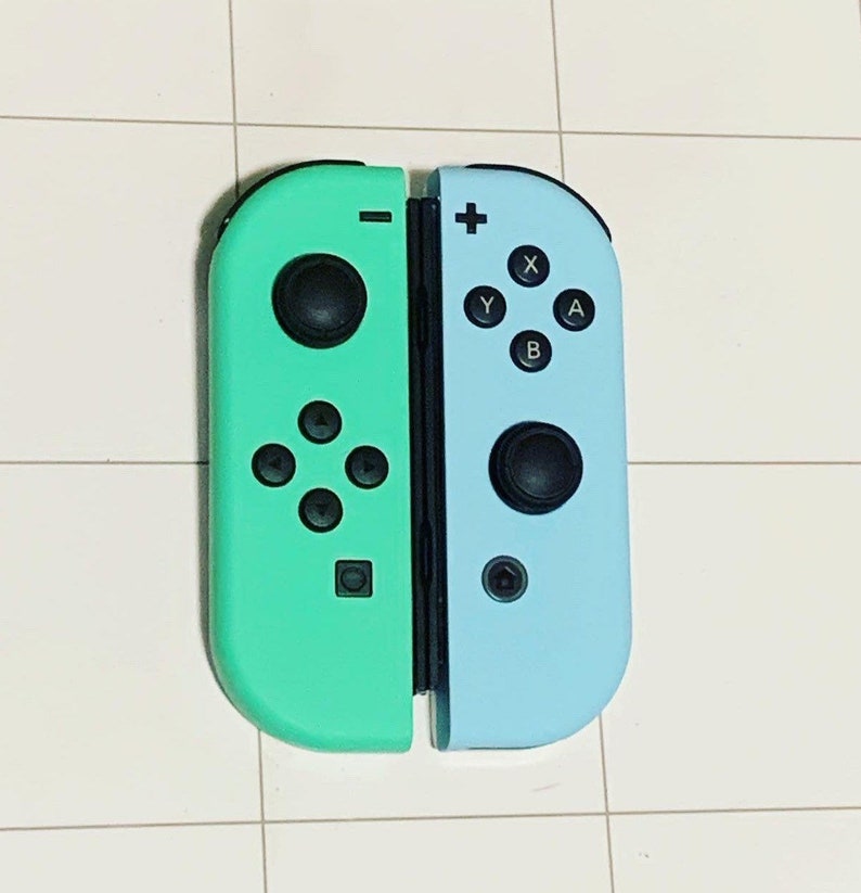 May include: A pair of teal and light blue Nintendo Switch Joy-Con controllers. The left Joy-Con is teal and the right Joy-Con is light blue. The controllers have black buttons and a black analog stick.