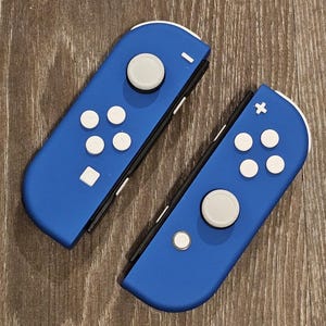 May include: Two blue Nintendo Switch Joy-Con controllers with white buttons. The left Joy-Con has a minus sign and the right Joy-Con has a plus sign.