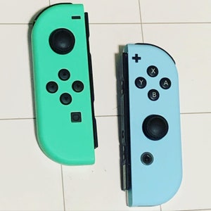 May include: Two Nintendo Switch Joy-Con controllers, one in a light blue color and the other in a light green color. Both controllers have black buttons and a black joystick.