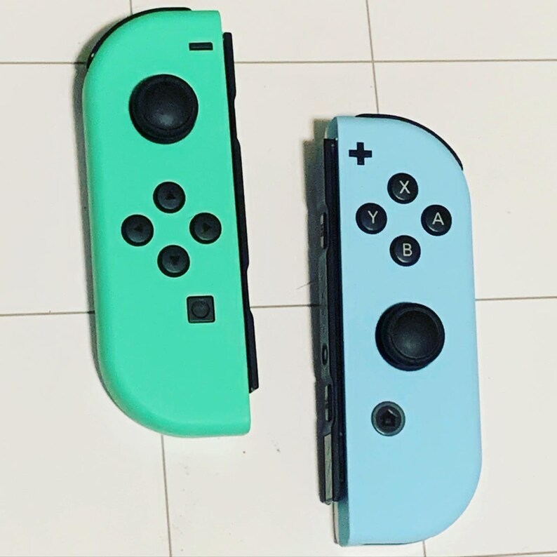 May include: Two Nintendo Switch Joy-Con controllers, one in a light blue color and the other in a light green color. Both controllers have black buttons and a black joystick.