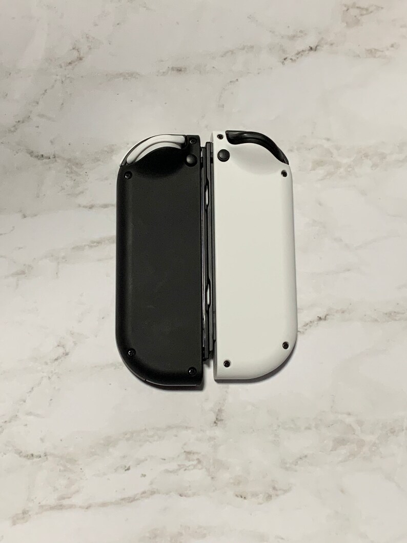 Puede incluir: Un par de mandos Joy-Con de Nintendo Switch, negro y blanco. El mando izquierdo es negro y el derecho es blanco.