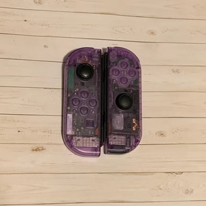 May include: A pair of purple transparent Nintendo Switch Joy-Con controllers. The controllers are separated and show the internal components.