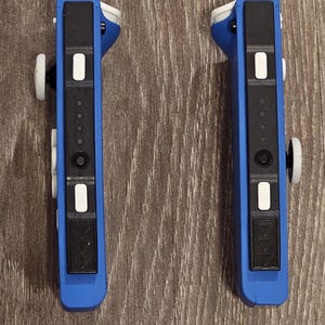May include: Two blue Nintendo Switch Joy-Con controllers with black buttons and white accents. The controllers are in a vertical position and have a black and white design.